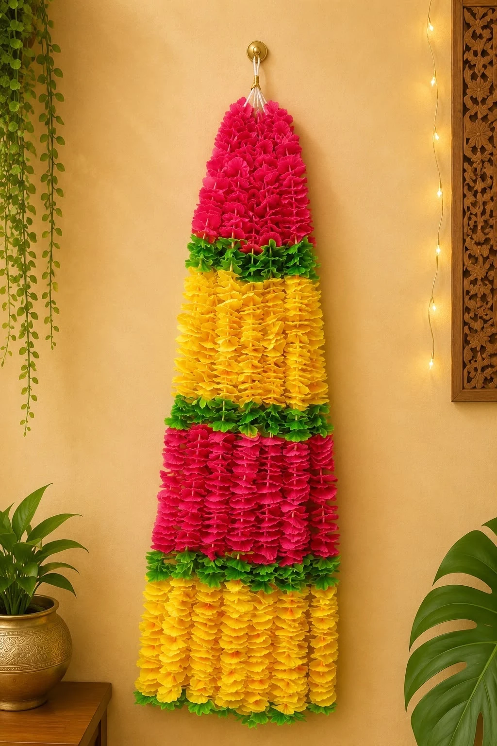 Pink and yellow tiered floral Diwali bandarwal with green leaf trim, hanging from a wall hook